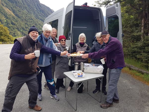 A tour group having a cup of tea and biscuit at one of the many nature stops on the way to Milford Sound