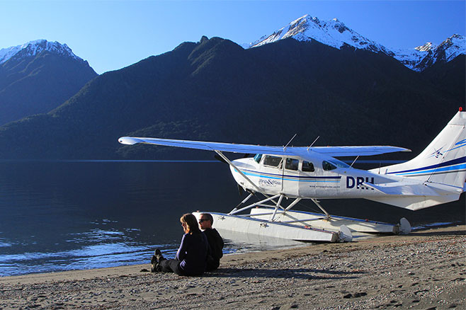 A couple of people sitting on a remote beach next to the float plane.